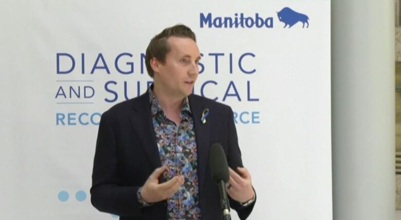 A man speaks at a microphone in front of a sign with the name of the provincial task force.