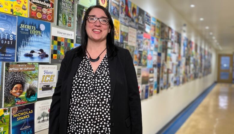 A woman stands in a hallway with brightly coloured posters lining the wall.