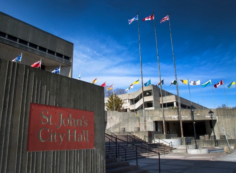 A stone building with a sign marking St. John's City Hall in the foreground. Flags are in the foreground.