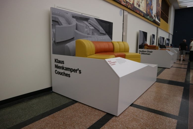 A display of a vintage yellow and orange couch in an airport exhibit.