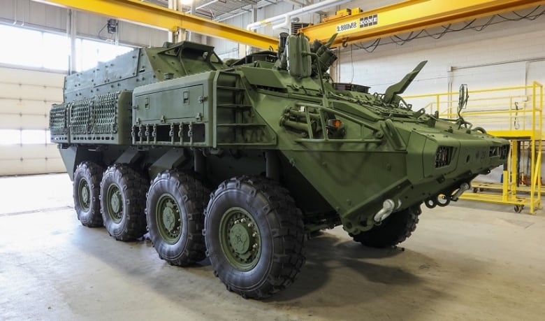 A large, green military vehicle with eight tires is parked inside a building near a large door.