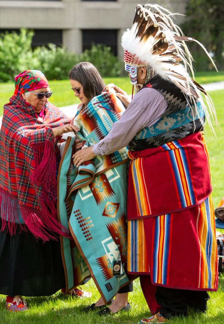 A woman with a tradditional blanket wrapped around her, given to her by two elders in tradditional Indigenous regalia.