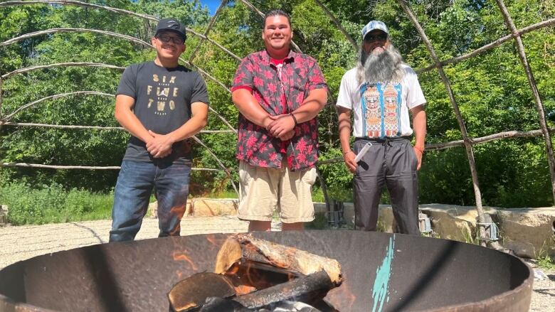 Three people stand behind a bowl with a fire burning inside it.