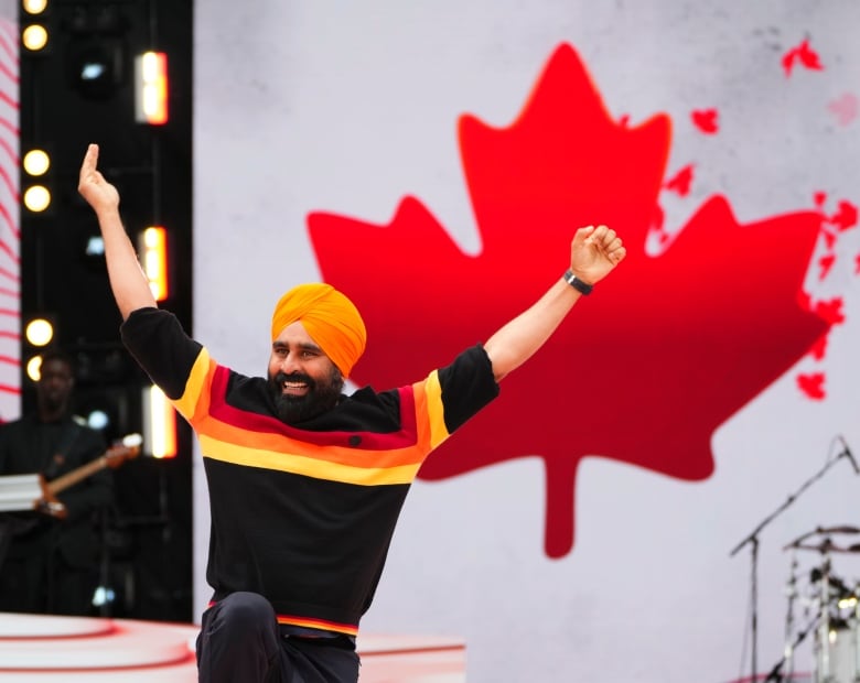 A man smiles while dancing in front of a Canadian flag.