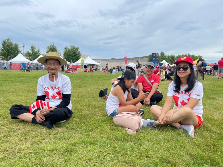 A family sits on a grassy field at a festival.