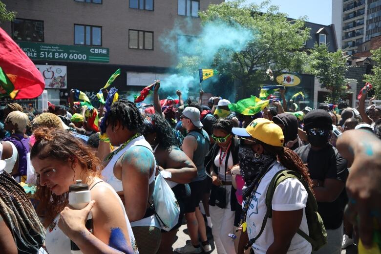 A crowd of Montrealers, many of them from the West-Indies, attend a parade along Saint-Catherine Street. Country flags can be seen being waved throughout the crowd. 