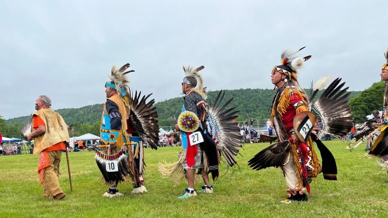 Four elders dressed in traditional regalia walk in a line. 