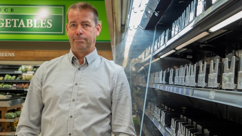 A portrait of a man standing in front of empty shelves at a store.