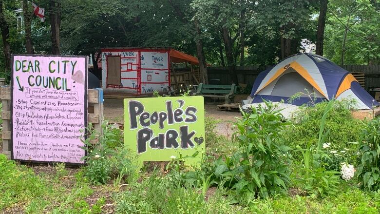 Image of tents and small structures in Meagher Park behind a signs that read 