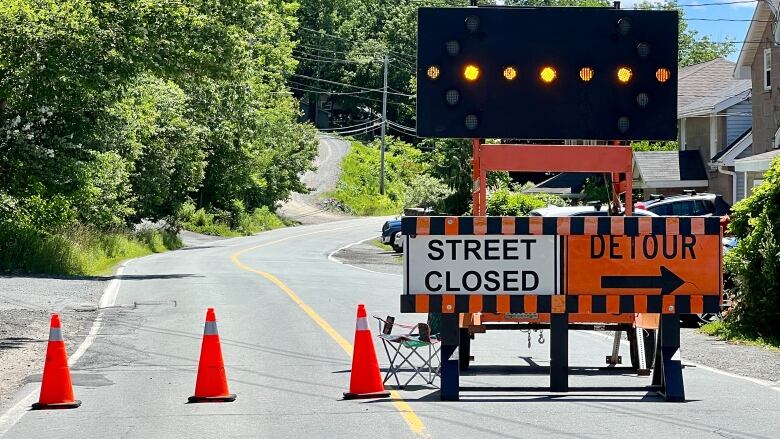 Traffic cones and detour signs close off a paved road. 