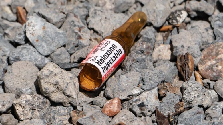 A closeup photo of a broken brown glass vial laying on gravel rocks.