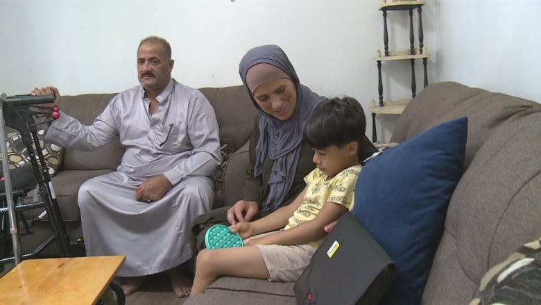 Three people, two adults and a child, pictured sitting down on a couch in a living room.