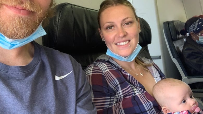 A selfie of a man and a women, with a baby in the lap of the women, on a plane.