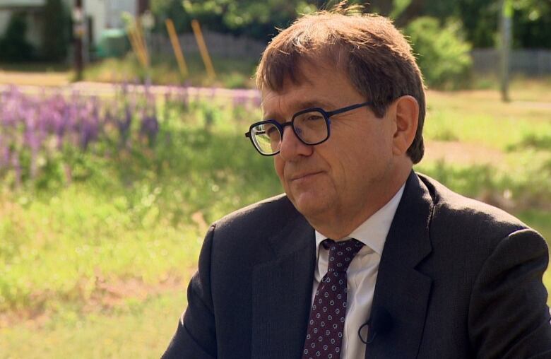 A man in a business suit sits in an open field. 