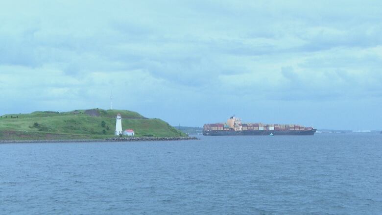 A wide shot of the Halifax Harbour. Part of George's Island is seen on the left, and a large cargo ship is in the water on the right.