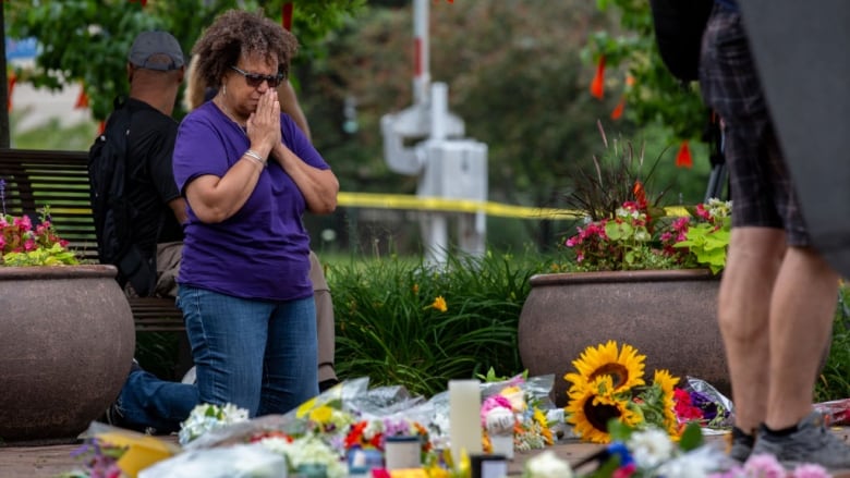 A woman kneels and prays at a sidewalk memorial.