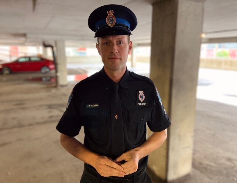 A Royal Newfoundland Constabulary officer wearing a uniform stands in a parking garage with his hands folded, looking at the camera.