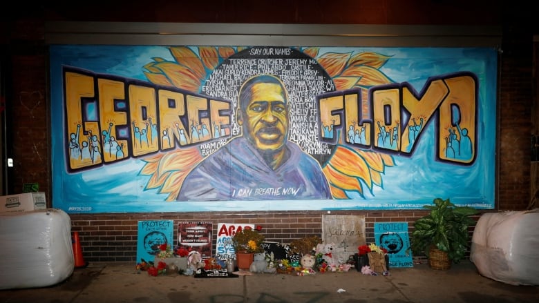 A mural painted on a brick wall depicts a Black man's face and the words 'George Floyd.' 