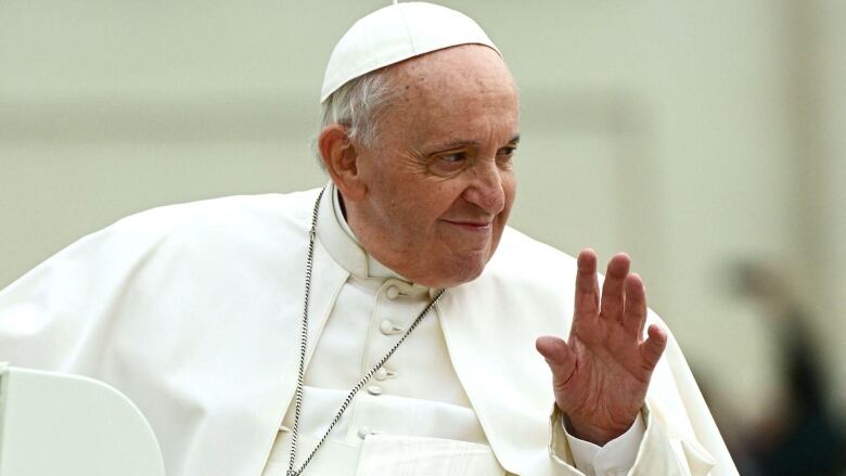 The pope sitting in his wheelchair and waving.