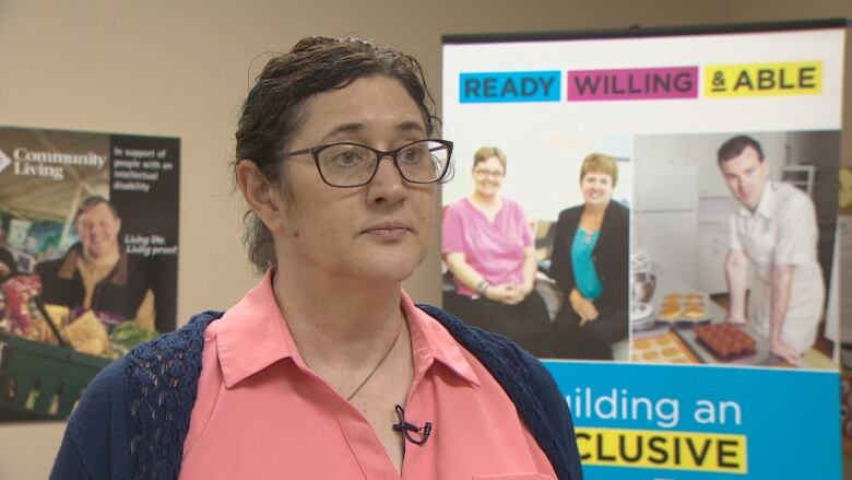 A woman stands in an office in front of posters promoting inclusivity.