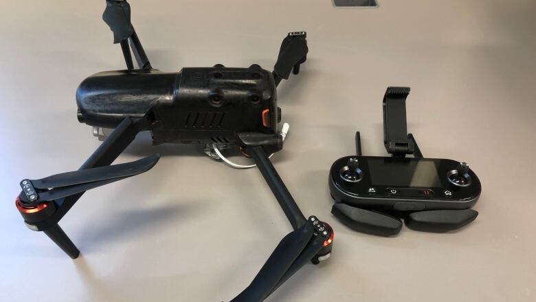 A black drone and remote control sit on a table.