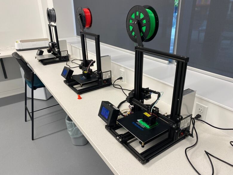 3D printers on a table. The one in the foreground is printing a green toy. 