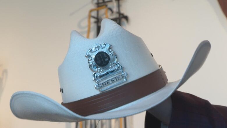 A white hat with a silver badge, with a legal scales symbol on them. The words 'Sherriff' are at the bottom of the badge.