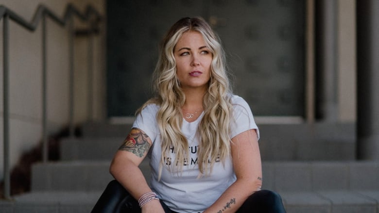 Alexandra Stevenson, founder of The Laughing Survivor, sits on a staircase, looking to her left.