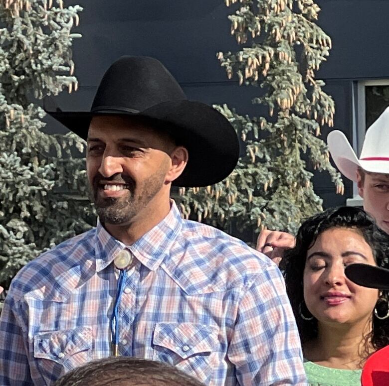 two men in cowboy hats and jeans speak to a crowd