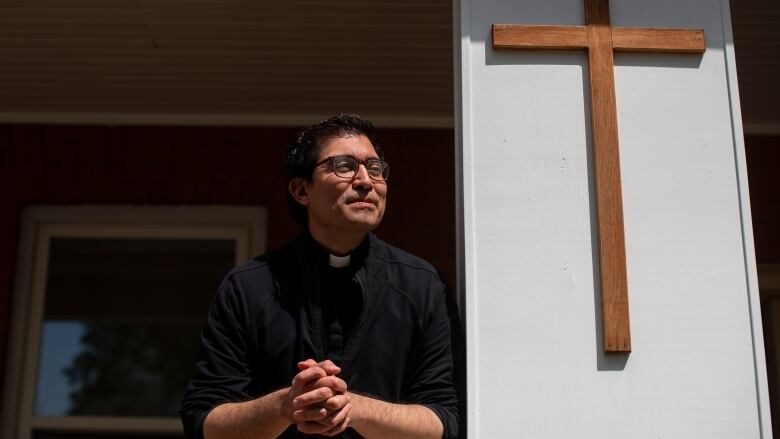 A man leans on a railing next to a giant cross. 