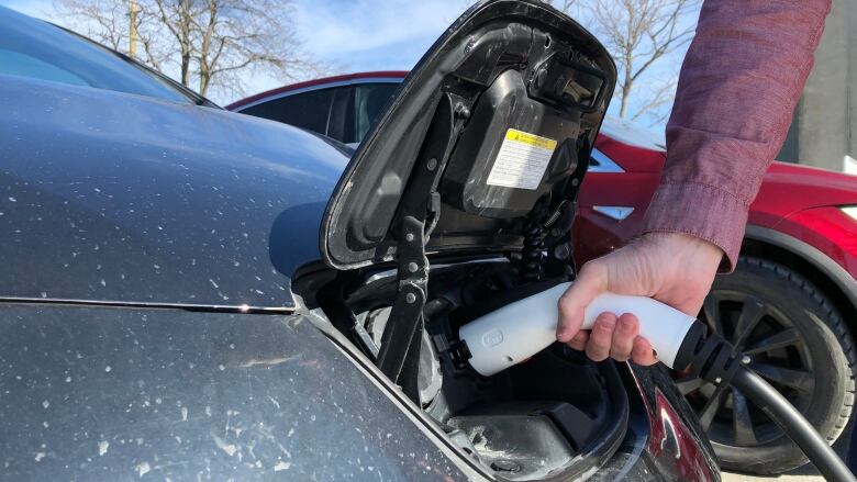 A closeup of a hand holding a charger plugged into the charging port of an electric vehicle.