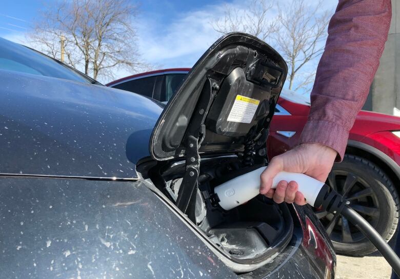 A closeup of a hand holding a charger plugged into the charging port of an electric vehicle.