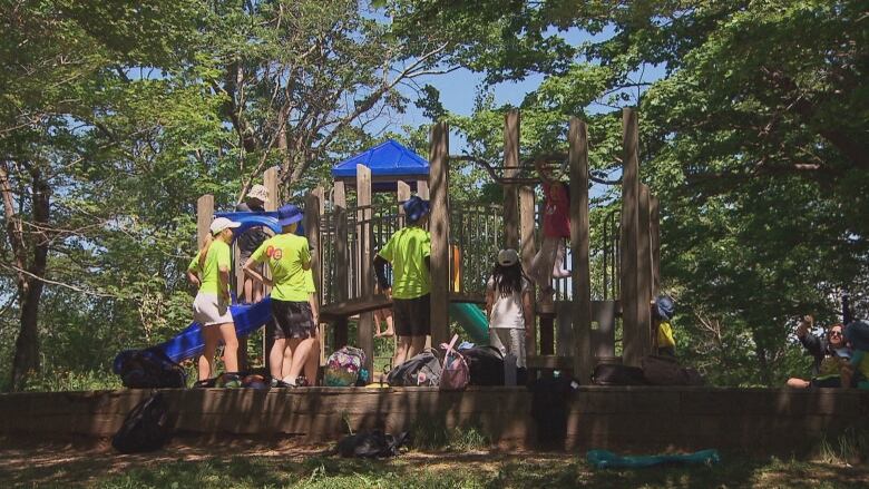 Camp staff members in fluorescent T-shirts monitor kids playing on a playground.