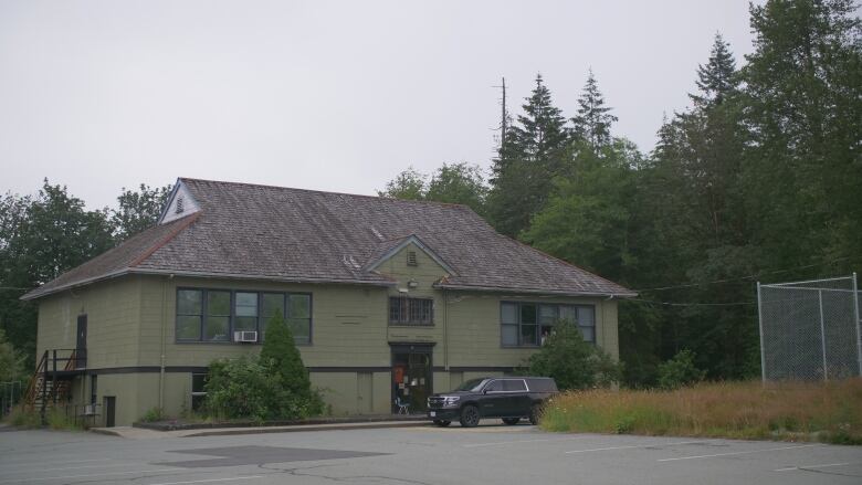 A green building stands in amongst trees. There is a black vehicle parked out front.