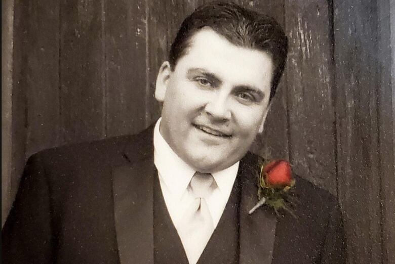 A portrait of a man wearing a formal suit with a red flower boutonnire on his suit jacket.