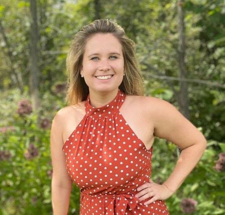 A woman stands in a copper dress with white polka dots in front of a tree