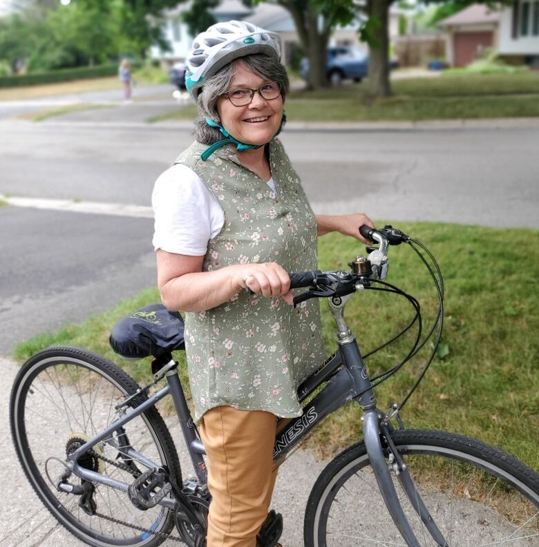 A woman wearing a bike helmet stands with her bike on a sidewalk.