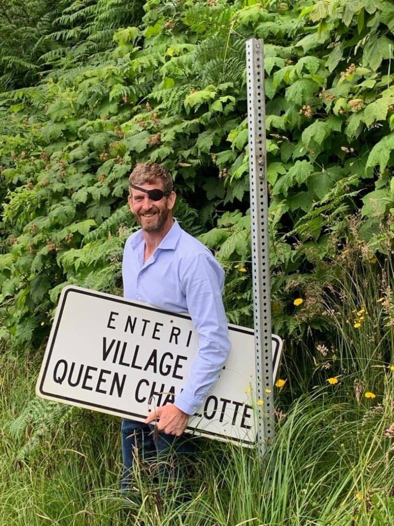 A man with an eyepatch carries a sign out of a ditch.