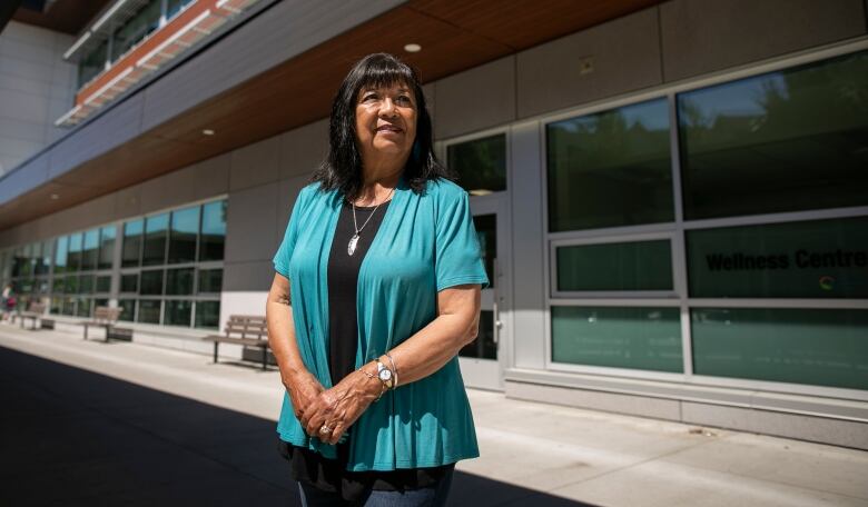 Rhonda Larrabee looks away from the camera. She is a middle-aged Indigenous woman wearing a blue dress.