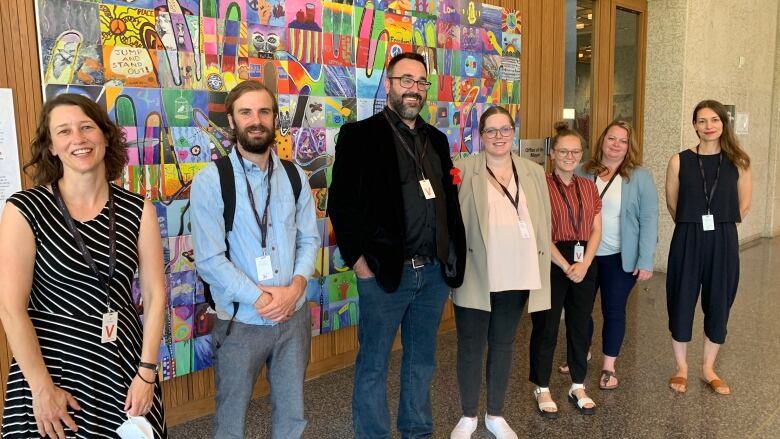 People stand in a line in front of a mural.