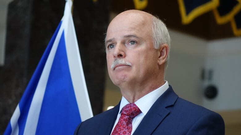 A man stands at the microphone during a press conference. He stands in front of a Newfoundland and Labrador flag.