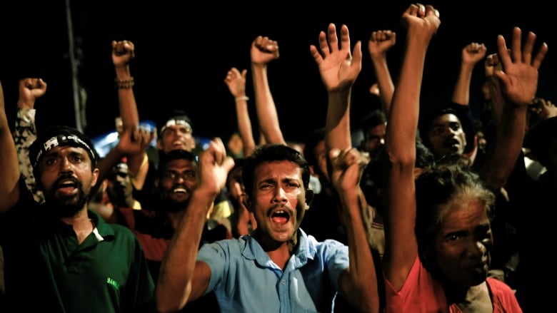 A group of people on a darkened street lift their arms in celebration.