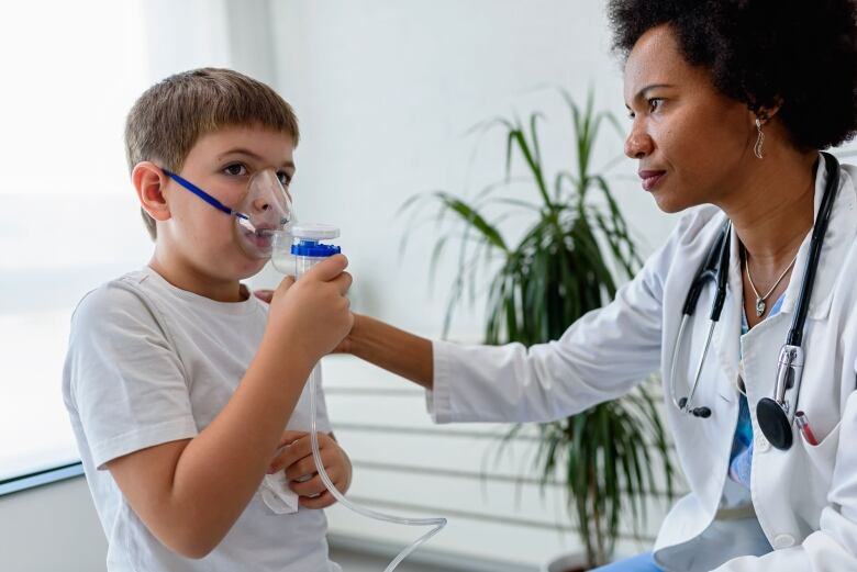 A child is using an inhaler. A doctor watches.