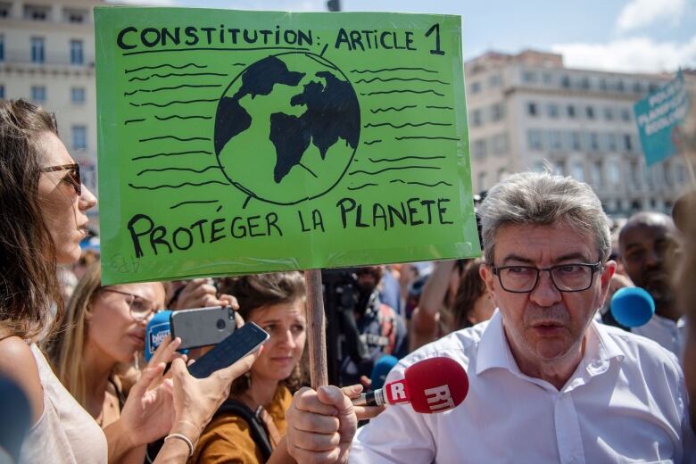 Environmental activists are gathered. One holds a sign saying 'Proteger la planete' (protect the planet, in French).