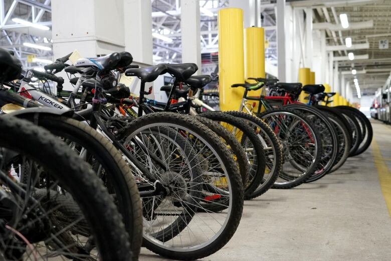 A row of different kinds of bikes are seen inside a garage-type facility.