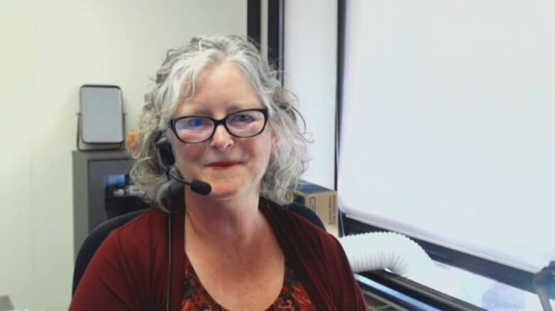 Woman with grey hair and headset on in an office looks at camera. 