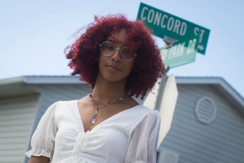 A girl with glasses and red hair looks into the camera in front of road signs that read Concord Drive and Highland Park Drive.