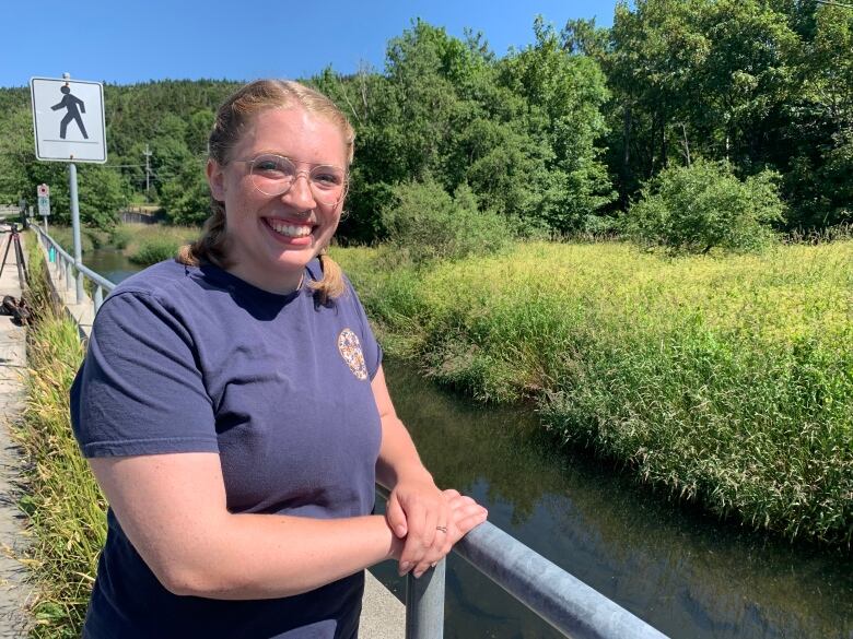 A woman wearing a purple T-shirt poses near the Waterford River in St. John's.