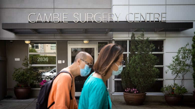 Two people in masks are pictured walking in front of the Cambie Surgery Centre in Vancouver in pictured on Friday, July 15, 2022.