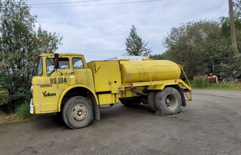 A bright yellow water truck is parked on a dirt road.